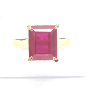 May include: A gold ring with a large, square, red gemstone.