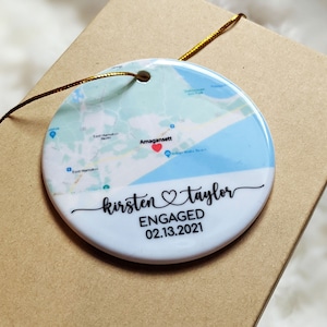 May include: A white ceramic ornament with a map of Amagansett, New York, featuring a red heart marking a location. The ornament is decorated with the text "kirsten ♡ taylor ENGAGED 02.13.2021".