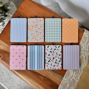 May include: Eight rectangular ID badge holders arranged in two rows. Patterns include blue stripes, colorful flowers, green gingham, orange polka dots, pink hearts, multi-colored stripes, baby footprints, and blue and pink vertical stripes.