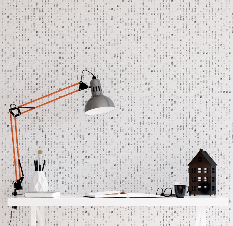 May include: A white wall with a black and white binary code pattern. A desk with a black and silver lamp, a white vase with pencils, a book, and a black house-shaped object.