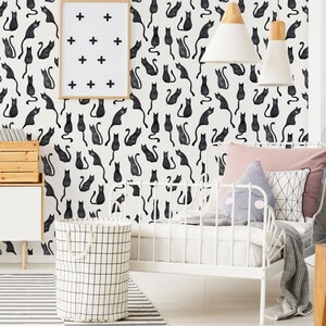 Puede incluir: Papel pintado con un patr&oacute;n repetitivo de gatos negros estilo acuarela sobre fondo blanco. El dise&ntilde;o incluye un cuadro con signos m&aacute;s negros, una estructura de cama de metal blanco, un cesto de ropa con patr&oacute;n de rejilla y cojines.