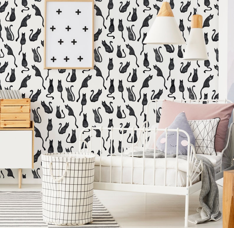 Puede incluir: Papel pintado con un patr&oacute;n repetitivo de gatos negros estilo acuarela sobre fondo blanco. El dise&ntilde;o incluye un cuadro con signos m&aacute;s negros, una estructura de cama de metal blanco, un cesto de ropa con patr&oacute;n de rejilla y cojines.