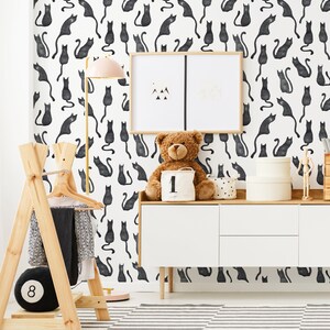 Puede incluir: Papel pintado con un patr&oacute;n repetitivo de siluetas de gatos negros sobre un fondo blanco. Los gatos aparecen en varias posturas sentadas y de pie, creando un dise&ntilde;o gr&aacute;fico monocrom&aacute;tico y denso en toda la superficie de la pared.