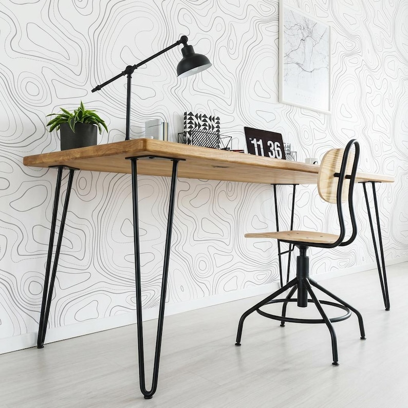 May include: A wooden desk with a light brown finish and black metal hairpin legs. On the desk sits a black adjustable desk lamp, a small green potted plant, a black and white patterned organizer, and a black digital clock displaying 11:36.