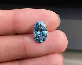 May include: A faceted, oval-shaped, blue gemstone. The gem is held between fingers, showcasing its brilliant cut and color. The stone's facets reflect light, creating a sparkling effect. The gem's color is a deep, vibrant blue.