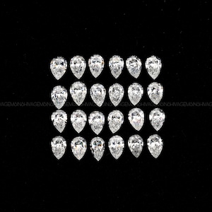 May include: Twenty-four pear-shaped diamonds are arranged in a grid against a black background. The diamonds are clear and sparkling, reflecting light. The gems are of similar size and shape, showcasing their brilliance.