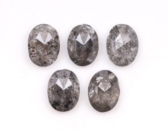 Pode incluir: Cinco pedras preciosas ovais e facetadas com uma aparência cinza salpicada. Cada pedra tem uma faceta triangular central. As pedras preciosas são dispostas sobre um fundo branco, mostrando suas texturas e cortes únicos. Ideal para fazer joias.