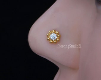 May include: Gold nose ring with a clear round stone surrounded by a circle of small gold beads.