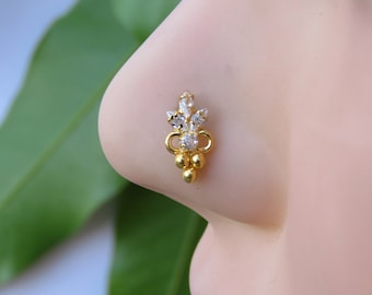 May include: A gold nose stud featuring a vertical arrangement of three clear marquise-cut stones at the top, a single round clear stone in the center, and three small gold spheres at the base, creating a decorative, multi-faceted design.