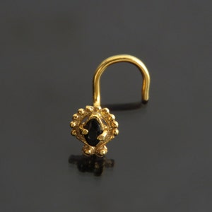 Pode incluir: Anel de nariz de ouro com uma pedra preciosa preta engastada em um design decorativo.