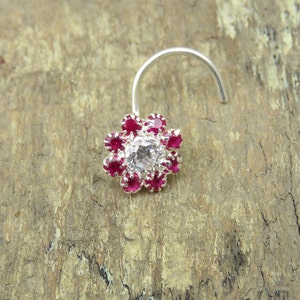 Könnte beinhalten: Ein silberner Nasenring mit einem weißen Edelstein, umgeben von einer Gruppe roter Edelsteine.