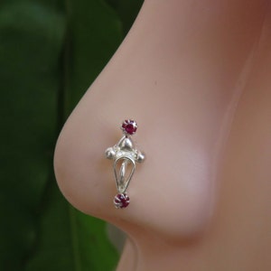 Op de afbeelding: Zilveren neusring met twee rode edelstenen. De ring heeft een decoratief ontwerp met een hangende lus.