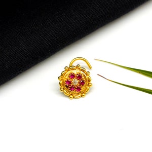 May include: A gold nose ring with a round design featuring a central white stone surrounded by pink stones.