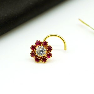 May include: A gold nose ring with a white stone in the center surrounded by red stones.