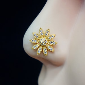 Op de afbeelding: Een gouden neusring met een bloemmotief met heldere strass steentjes.