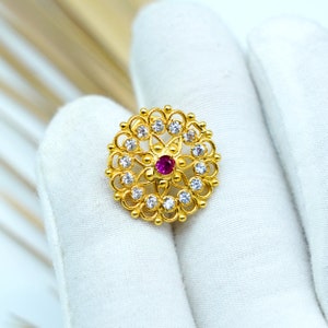 Peut inclure: Une bague en or avec un motif circulaire orné d'une pierre précieuse rose entourée de petites pierres blanches.