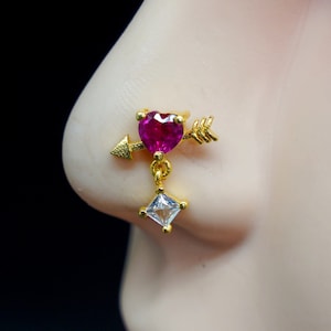 May include: Gold nose ring with a pink heart and arrow charm, and a dangling square clear stone.