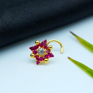 Puede incluir: Anillo de nariz de oro con un diseño en forma de estrella que presenta una piedra blanca central rodeada de piedras rosas.