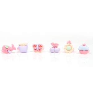 May include: Six colorful plastic rings with different cartoon designs: a whale, a french fry container, a butterfly, a cherry, a sunflower, and a cupcake.