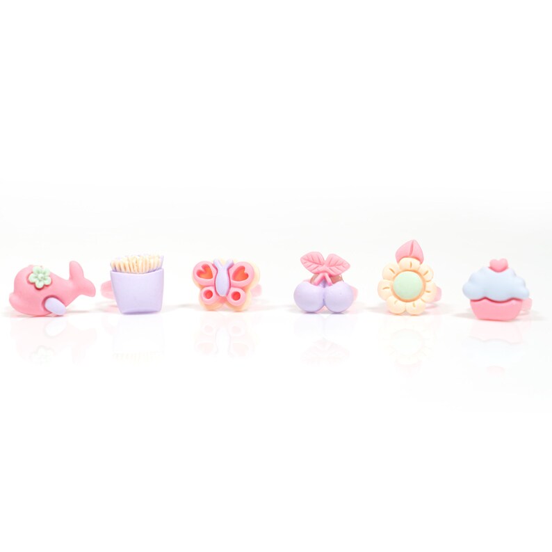 May include: Six colorful plastic rings with different cartoon designs: a whale, a french fry container, a butterfly, a cherry, a sunflower, and a cupcake.