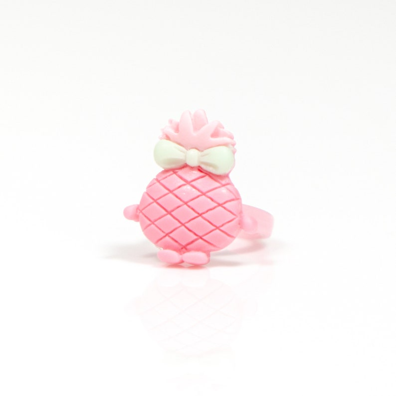 May include: A pink plastic ring with a pineapple design. The pineapple has a white bow and a green top.
