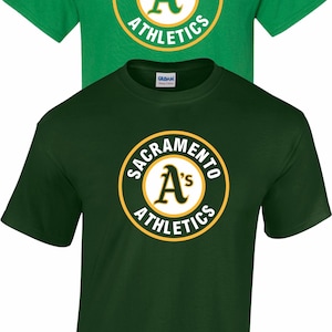 May include: Two short-sleeved t-shirts, one green and one dark green, featuring the "Sacramento Athletics" logo. The logo is a circular design with the letter "A" in the center, surrounded by text in a yellow and white color scheme.