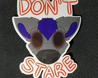 May include: A sticker featuring a stylized cartoon animal face with gray fur, purple accents, and bloodshot eyes. The text "DON'T STARE" is written in red, outlined letters above and below the face.