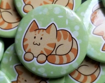 May include: A collection of round, green cat-themed buttons. Each button features a cartoon orange tabby cat with brown stripes, lying down on a light green background with white polka dots. The buttons are scattered across the image.