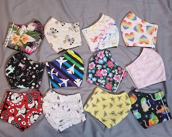 May include: Assortment of face masks with various patterns. Designs include floral, cartoon characters, rainbow hearts, sewing notions, airplanes, marble, bees, cats, and a pink solid color. Each mask has elastic ear loops for secure wear.