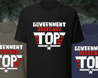 May include: Three short-sleeve t-shirts in black, olive green, and navy blue. Each shirt features the text "GOVERNMENT ASSIGNED TOP" in a bold, white, and red design with a star at the bottom. The shirts are displayed against a star-patterned background.