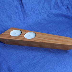 May include: A wooden candle holder with two candle wells. The holder is made of light brown wood and has a pointed end.