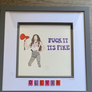 May include: Framed artwork featuring a drawing of a woman holding a red megaphone, with the text "FUCK IT IT'S FINE" in purple. The name "OLIVIA" is spelled out in letter tiles below the artwork.
