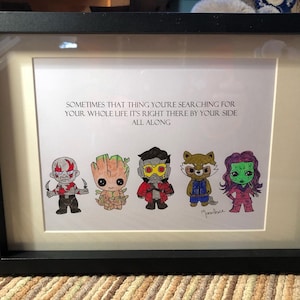 May include: Framed print with a quote about finding what you're looking for: "Sometimes that thing you're searching for your whole life it's right there by your side all along."  The quote is illustrated with cartoon characters from the Guardians of the Galaxy movie.