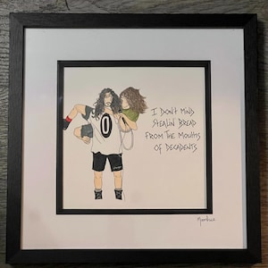 May include: Framed artwork with a drawing of two people, one carrying the other. The person being carried holds a microphone. The artwork includes the text: "I DON'T MIND STEALIN' BREAD FROM THE MOUTHS OF DECADENTS." The artwork is signed.