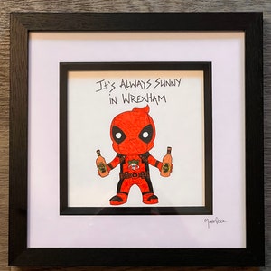 May include: A hand-drawn illustration of a red and black Deadpool character holding two bottles of alcohol. The text "It's Always Sunny in Wrexham" is written above the character. The artist's signature "Moonface" is in the bottom right corner.