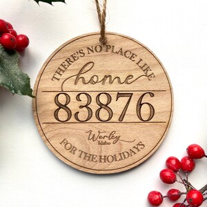 Könnte beinhalten: Ein runder Holzanhänger mit dem eingravierten Text "There's no place like home 83876 Worley Idaho for the holidays".