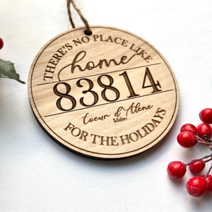 Puede incluir: Un adorno redondo de madera con el texto "There's no place like home 83814 Coeur d'Alene Idaho for the holidays".