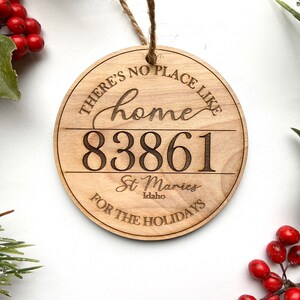 以下が含まれることがあります： 「There's no place like home 83861 St. Maries Idaho for the holidays」という文字が刻まれた丸い木製のオーナメントです。