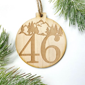 May include: Wooden Christmas ornament with a mountain and forest scene and the number 46.
