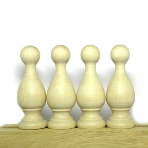 Könnte beinhalten: Vier unbemalte, tropfenförmige Holz-Abschlusskappen mit abgerundeten Oberseiten, in einer Reihe auf einer Holzoberfläche angeordnet.