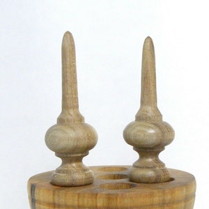 May include: Two wooden finials with a pointed top and a rounded base. The finials are sitting on a wooden base.