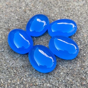 May include: Five smooth, oval-shaped blue agate stones arranged in a circle on a gray, textured surface.