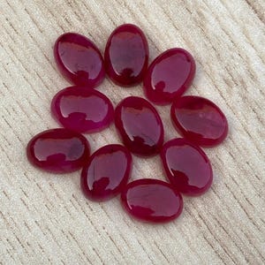 Peut inclure: Dix pierres précieuses roses de forme ovale, taillées en cabochon. Les pierres précieuses sont disposées en cercle sur une surface en bois brun clair.