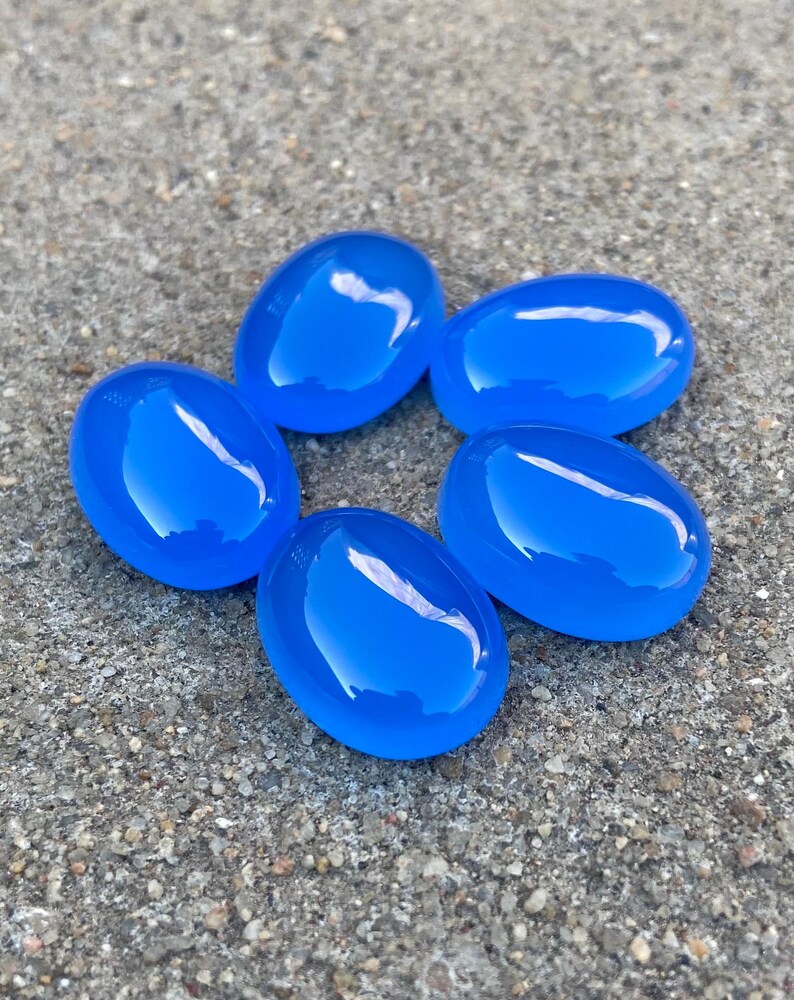 May include: Five smooth, oval-shaped blue agate stones arranged in a circle on a gray, textured surface.