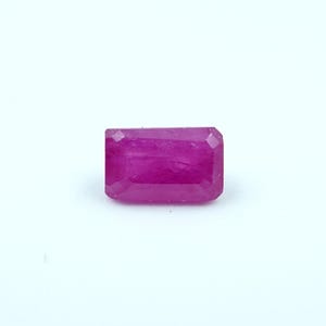May include: A rectangular-cut, vibrant magenta gemstone. The gem has a faceted surface, catching light and showcasing its rich color. The stone is set against a plain white background, highlighting its clarity and brilliance. This gemstone is suitable for jewelry.