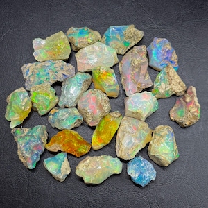 May include: A collection of raw, unpolished opal stones featuring irregular shapes and rough, earthy textures. Each stone displays a unique play of color, including flashes of neon green, vibrant orange, electric blue, and soft pink against a milky base.