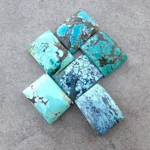 Peut inclure: Une collection de huit cabochons en turquoise, chacun avec un motif unique de bleu, vert et noir. Les cabochons sont taillés en forme carrée et sont disposés en quinconce.