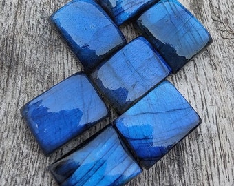 May include: Seven polished, dark blue labradorite stones, each cut into a rectangular shape, arranged in a staggered pattern on a wooden surface.