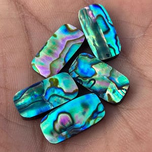 May include: Five iridescent abalone shell cabochons in rectangular shapes with a dark green, blue, and purple colour pattern.