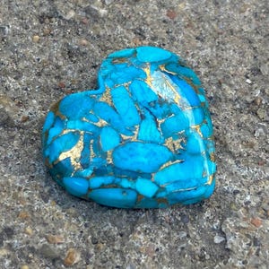 May include: A heart-shaped turquoise stone with gold veins. The stone is a deep blue colour and has a smooth, polished surface.